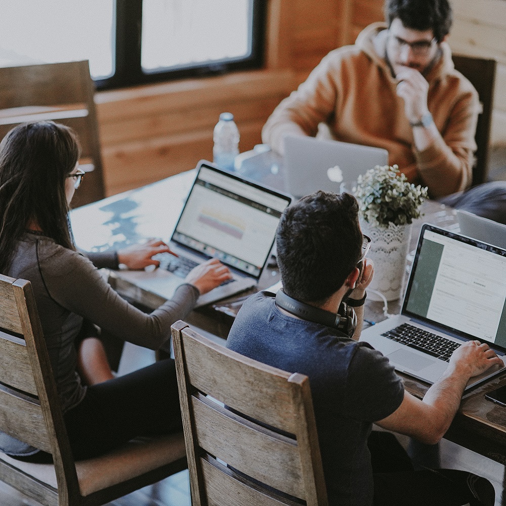 Three people sitting at a desk all working on computers.