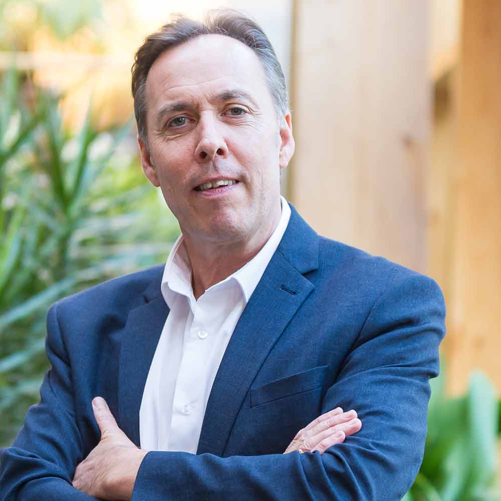 John Niland, wearing a blue suit and white shirt, with arms folded