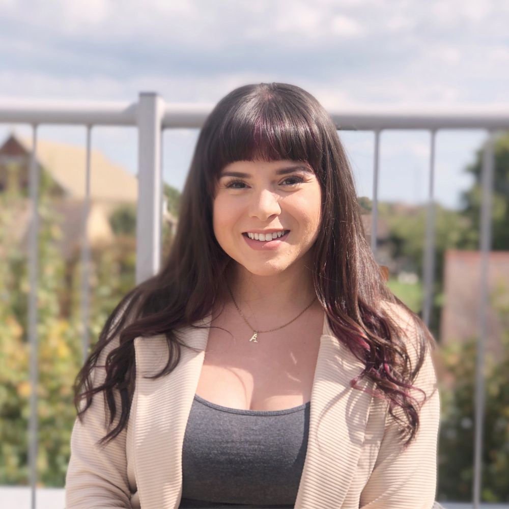 Alicia Torres, who studied MSc International Marketing and Entrepreneurship, stands on a balcony. She is smartly dressed, and she is stood smiling directly towards the camera. 