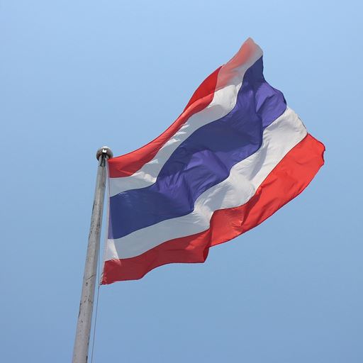 The flag of Thailand (red, white and blue horizontal stripes) flying against a blue sky.