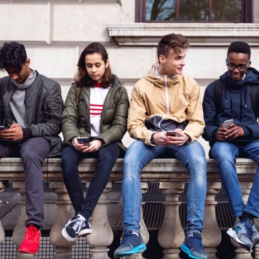 Picture of four young people sitting on a  wall, chatting and checking their phones