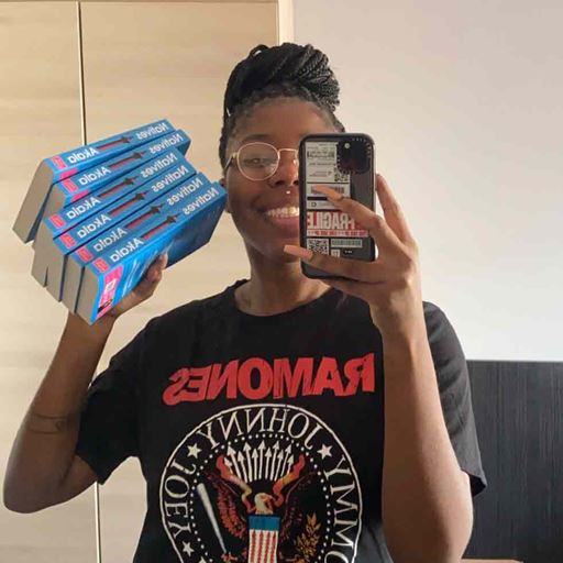 Maja Antoine-Onikoyi taking a selfie of herself holding a stack of books in one hand and her phone in the other.