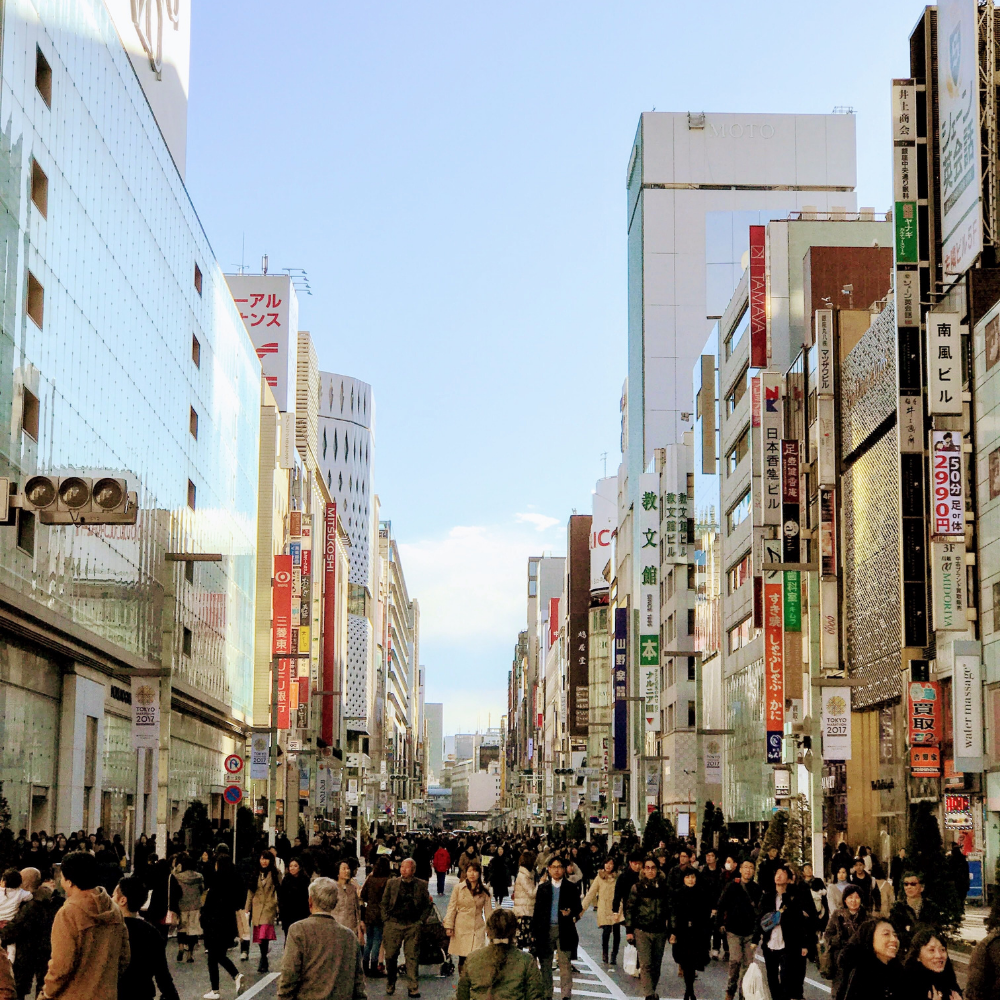 Photo of people walking across a busy street. High-rise buildings feature in the background