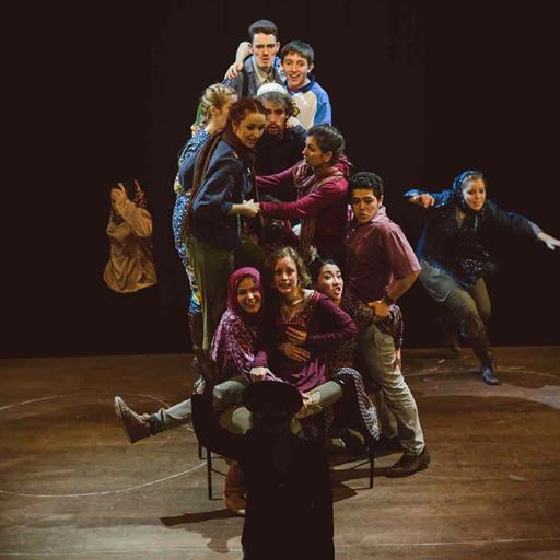 A group of actors, on a stage, all piled on top of each other