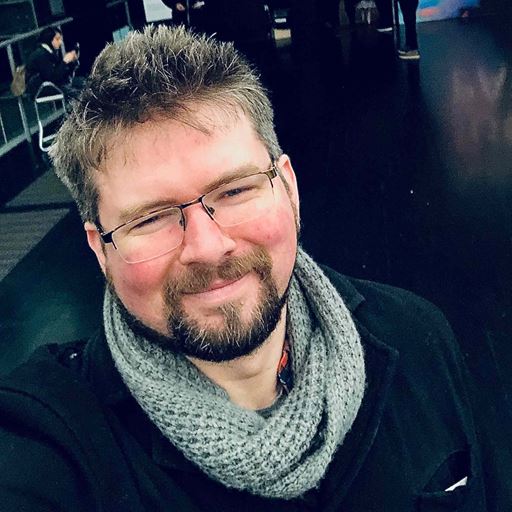 Dr Liam Jarvis, smiling, wearing glasses, a grey scarf and black coat