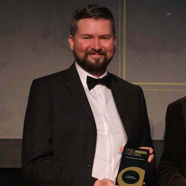 Dr Liam Jarvis wearing a black bow tie, white shirt and black jacket and holding his Times Higher Education award