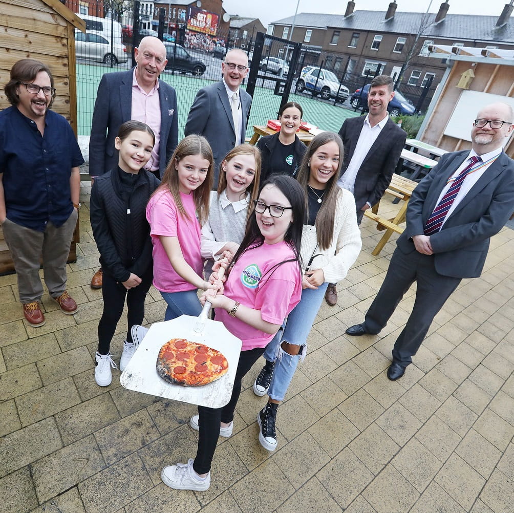 image of group of people including 5 young women who are showing a pizza just out of an outdoor oven