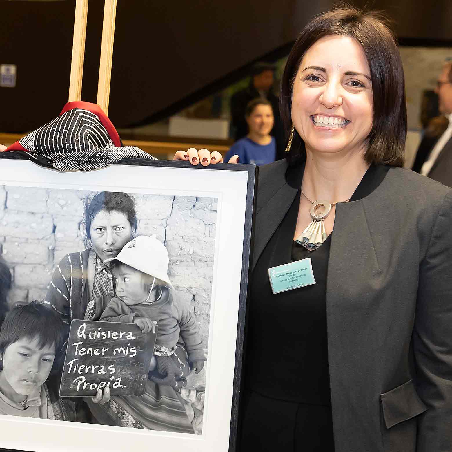 Professor Mariachiara Di Cesare stands next to a framed black and white photograph of a mother and two children