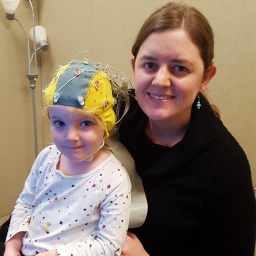 Photo of woman with young child on her lap who wears an EEG cap