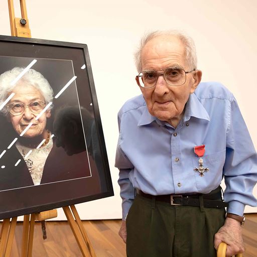 Frank Bright MBE, standing next to a framed portrait of Dora Love
