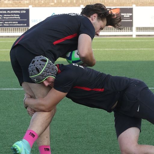 photo of two rugby players in a tackle, one with a headset on, one without