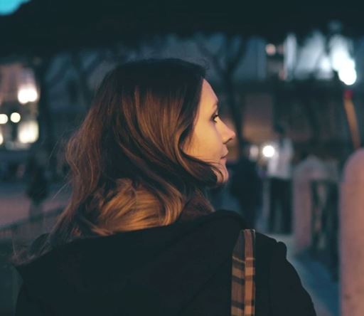 Back of a woman's head walking at night towards a building (which is blurred in the background)
