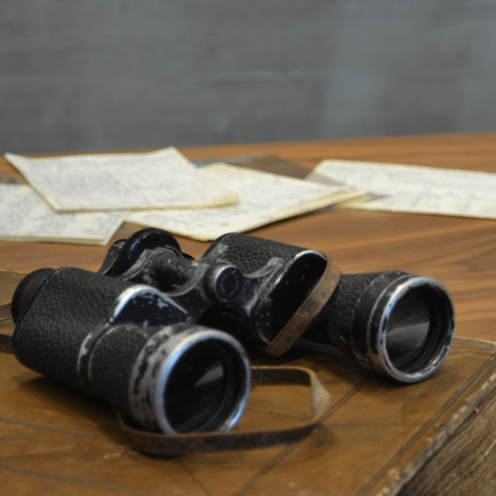 A pair of black binoculars and some paperwork on top of a table