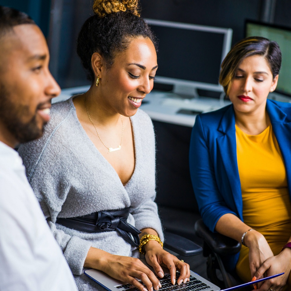 A group of employees sit in chairs in front of a laptop, signifying equality and inclusion at work.
