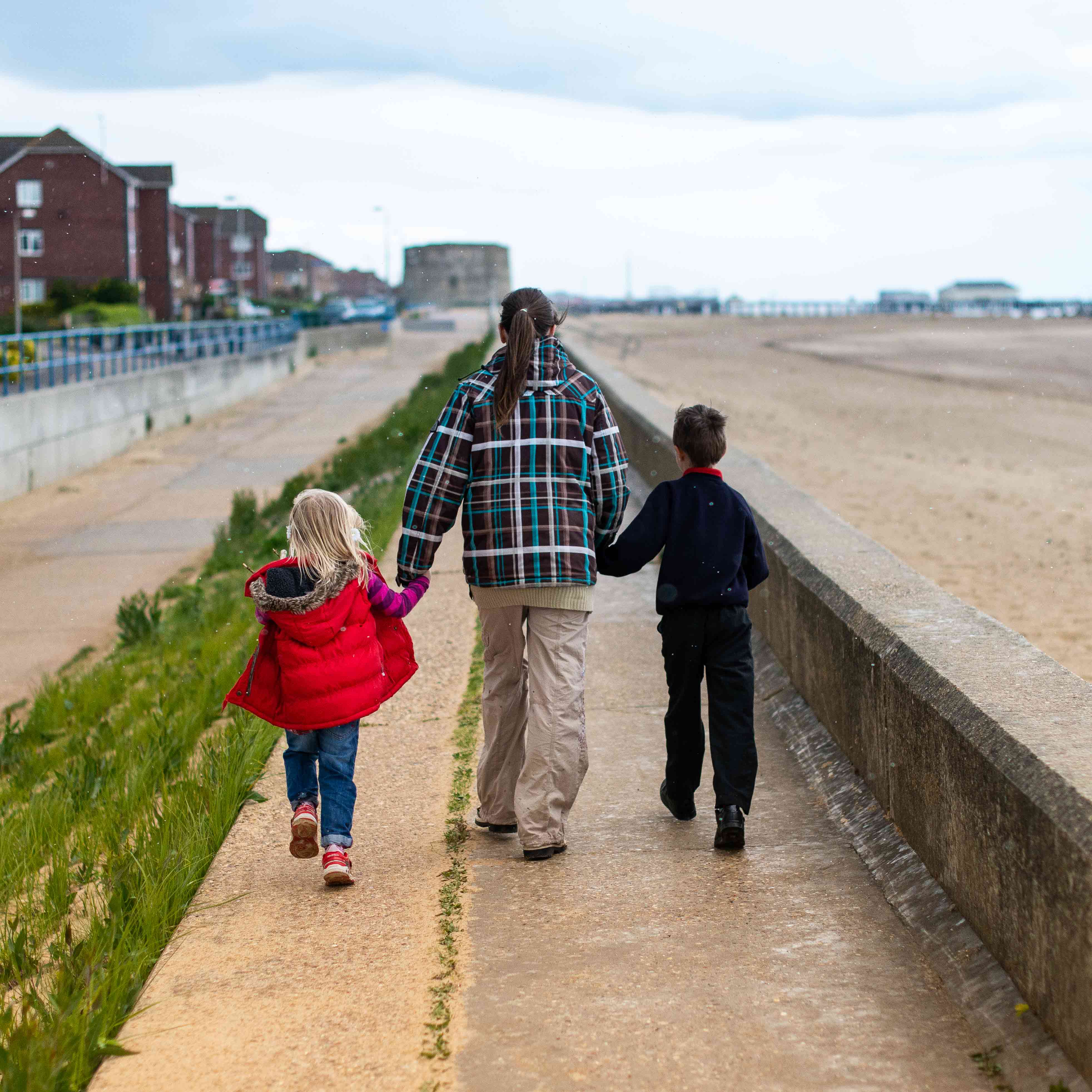 A woman and two young children walk along a seafront path in Jaywick, Essex