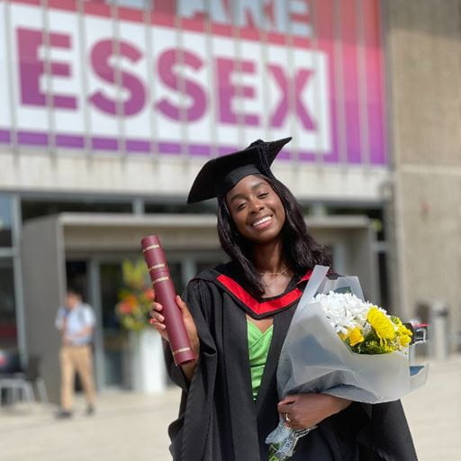 Graduate with flowers and degree certificate in front of Lakeside Theatre