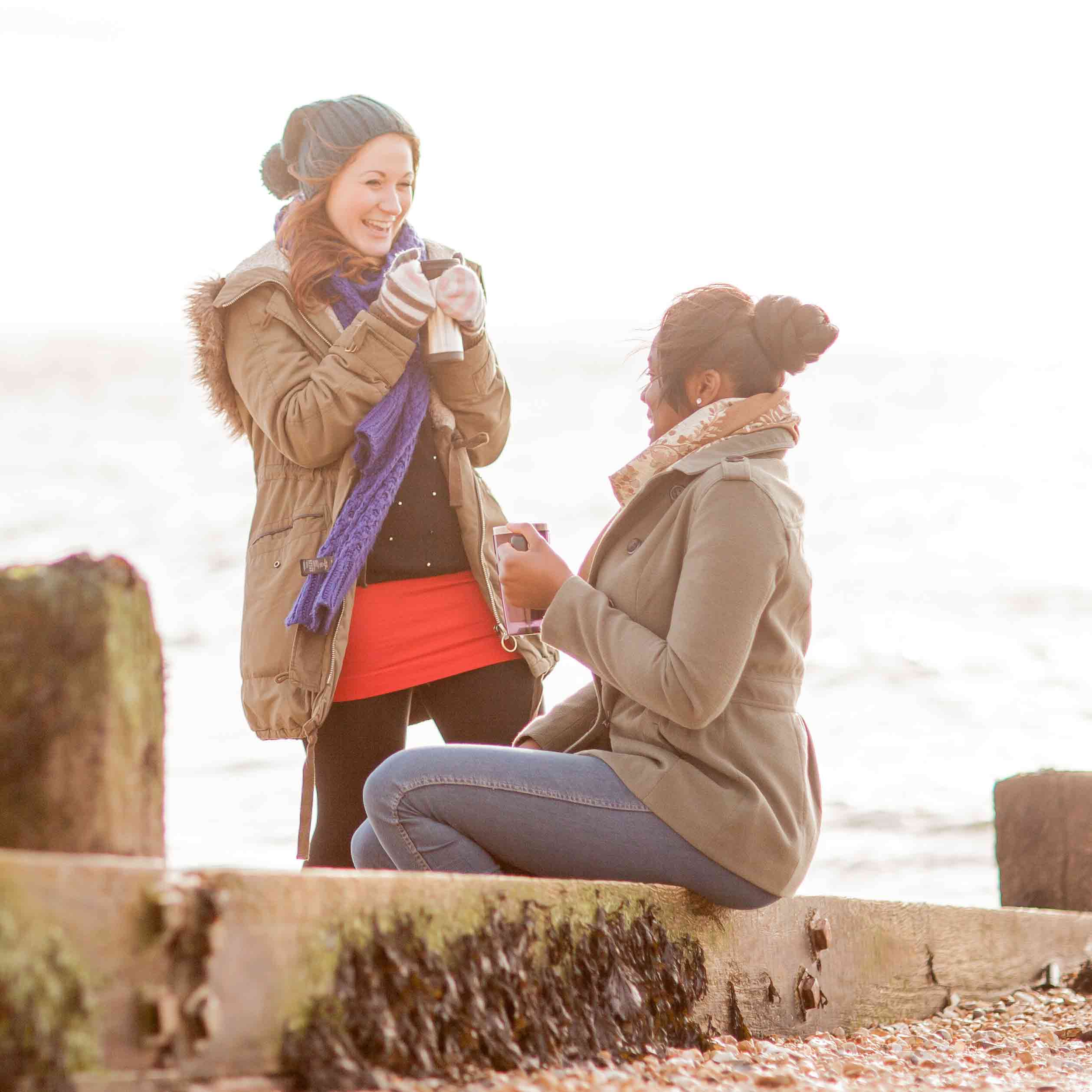 Two young women on a beach on a bright, cold winter day laughing and looking relaxed