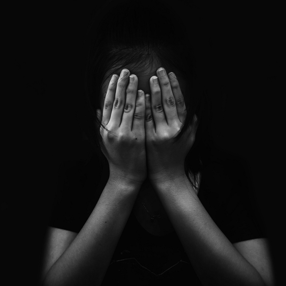 A black and white image of a person clutching their hands over their face.