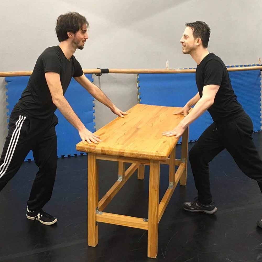 Andrea Lavio and Mateus Monteiro, both wearing black, standing on either side of a wooden table, facing one another