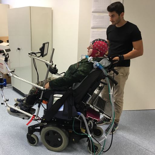 Man in wheelchair with EEG cap on with researcher 