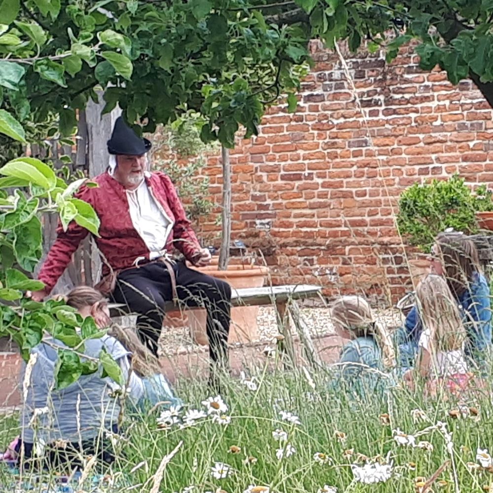 A man dressed up telling a story to children and a parent in a field (an event at Essex Book Festival)