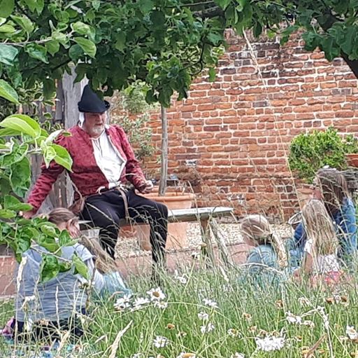 A man dressed up telling a story to children and a parent in a field (an event at Essex Book Festival)