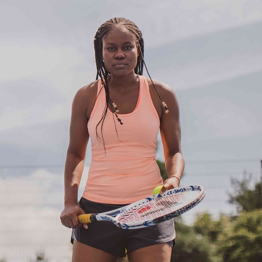 A young woman, looking serious and wearing fitness clothing holds a tennis racket and stares straight at the camera