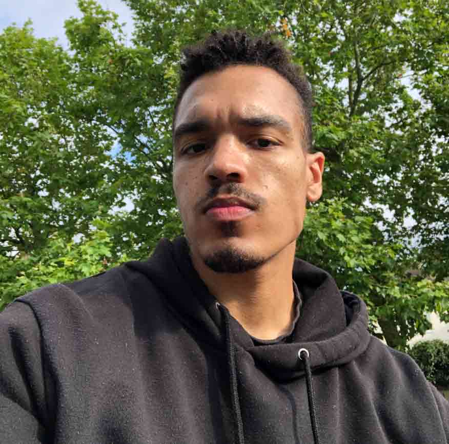 Nicholaus Harrington staring intently at the camera against a green, leafy background