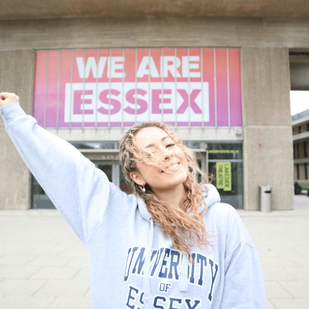 We Are Essex sign with student smiling in our University hoodie
