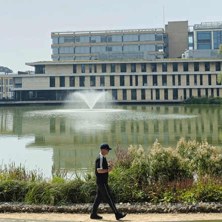 View of Silberrad Student Centre across the lake with man walking at the front