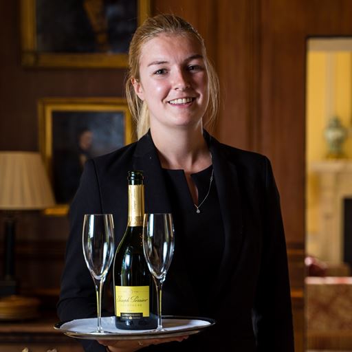 Former Edge Hotel School student Ellie Dimes holding a tray of drinks in her role as Restaurant Manager at Lucknam Park