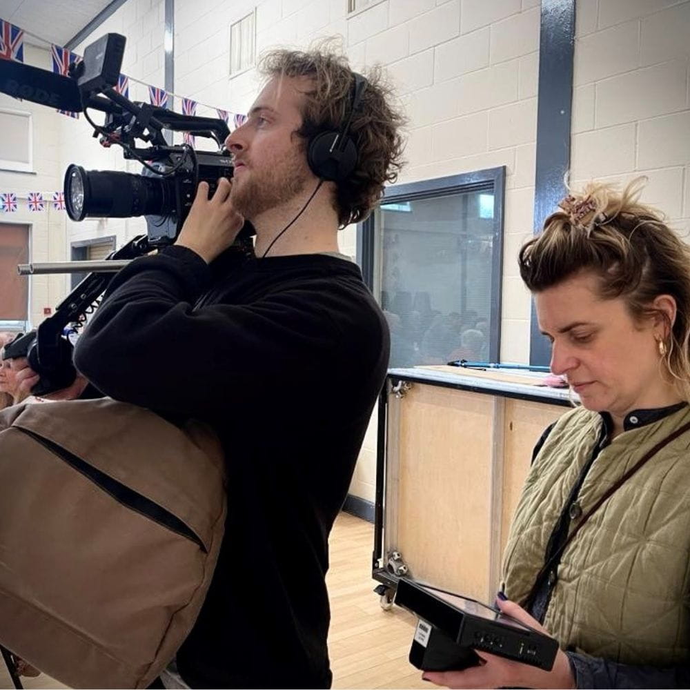 Two filmmakers at work on the Greenstead estate in Colchester, one holds a camera while the other looks down at a mobile device