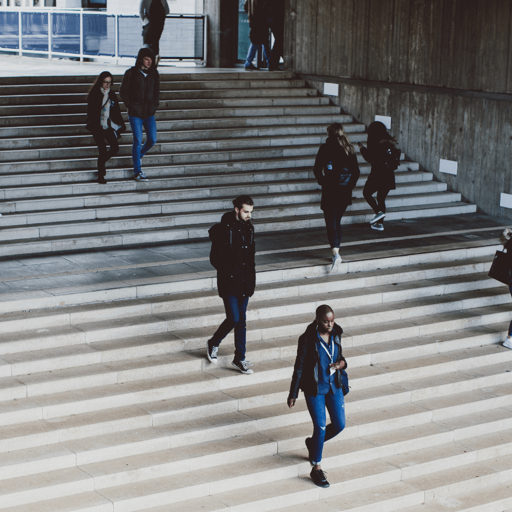 A group of people walk seperately or in small groups down some wide grey stepss