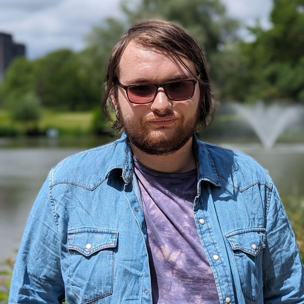 Joshua Mullett wearing dark glasses and standing in front of a lake