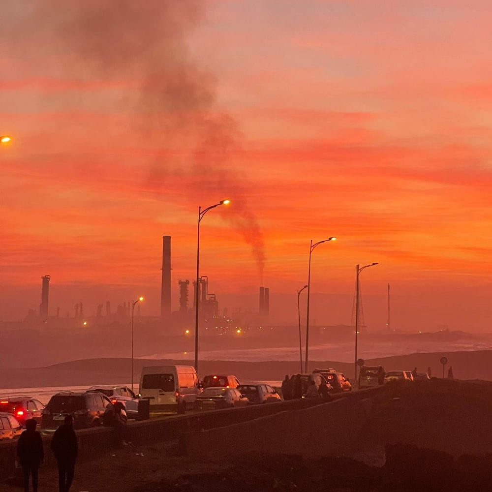 A hazy, glowing red smoked-filled sky with chimneys in the distance