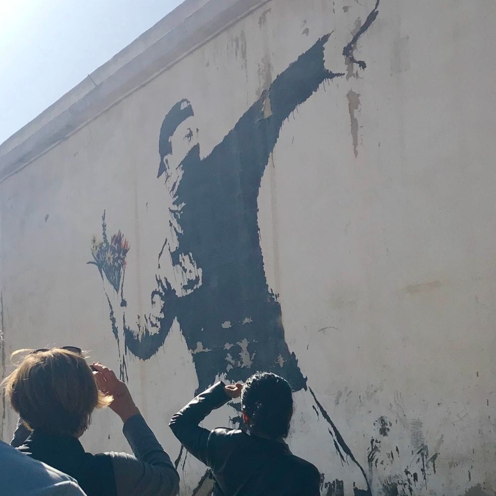 Tourists take photos of the Flower Thrower, by Banksy