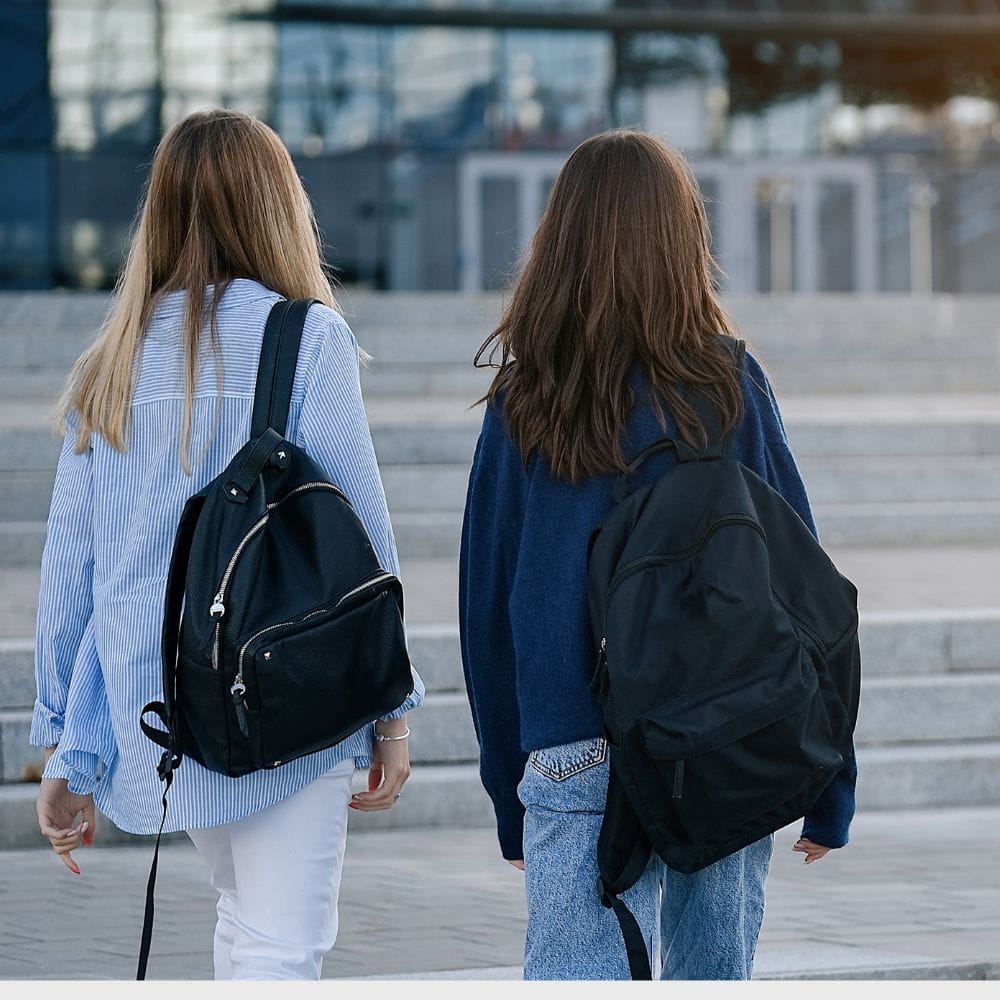 Two teenage girls, seen from behind, carrying rucksacks