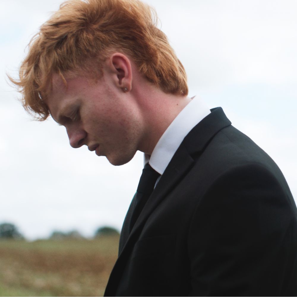 A young man, wearing mourning clothes, bows his head. A still from the short film Roadside Funeral, written and directed by Marty Pritchard.
