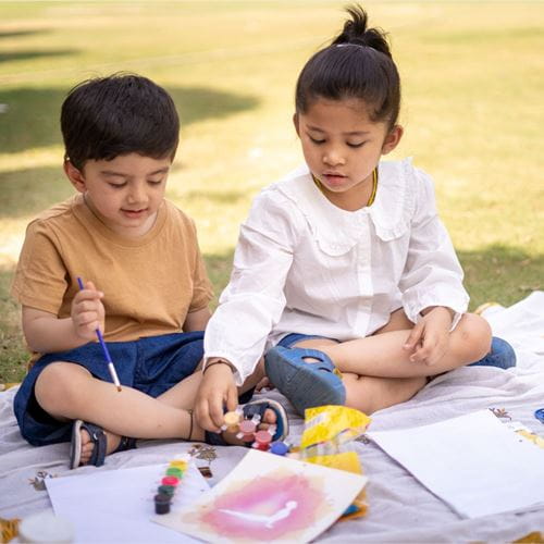 Children outside sitting on grass painting