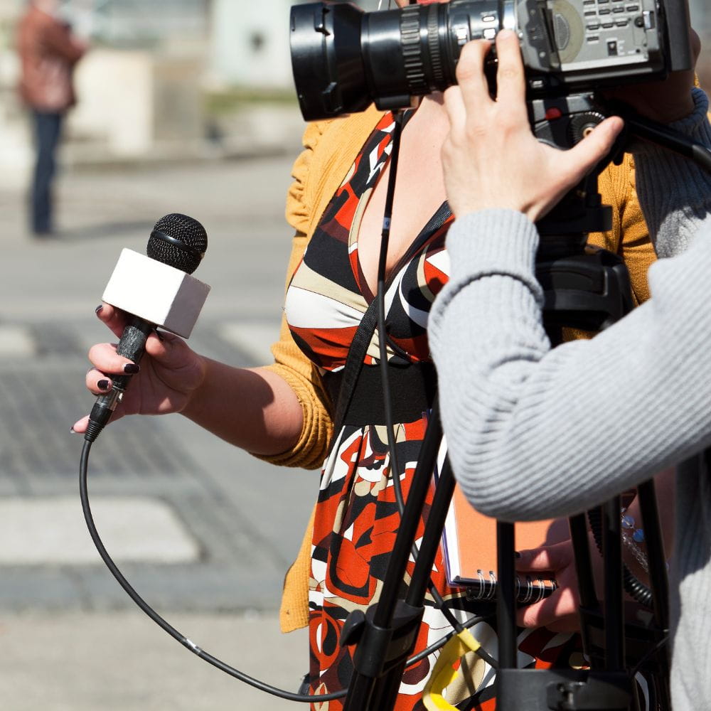 Female journalist holding a microphone alongside a cameraman