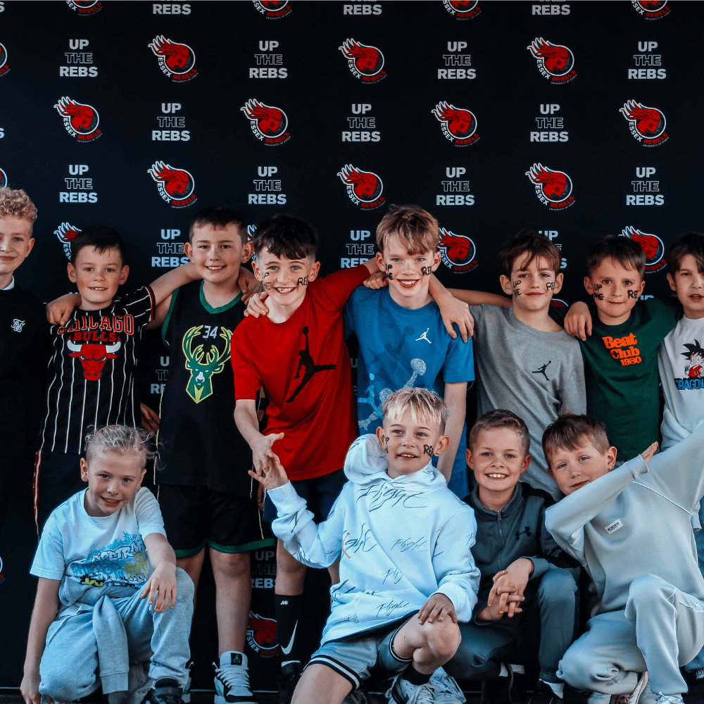 Group of kids lined up outside with the logo background of the Rebels