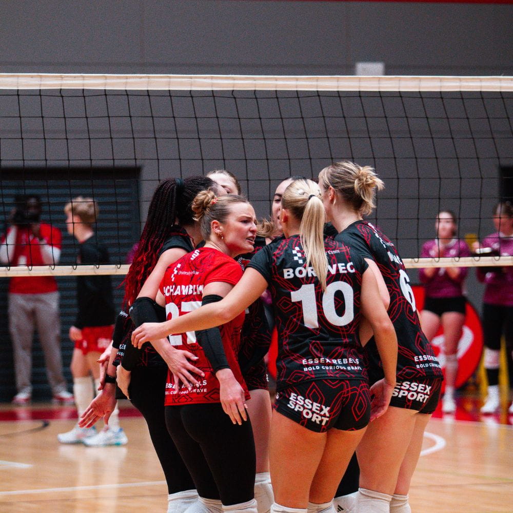Women's Rebels Volleyball players huddled together in front of the net 