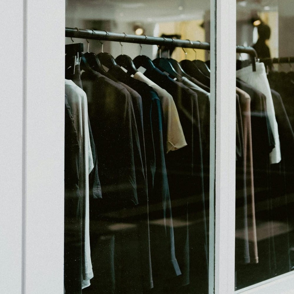 A rack of clothes on the other side of a window with a white frame.