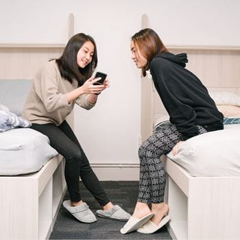 Two female students in accommodation sitting on the beds and looking at a phone