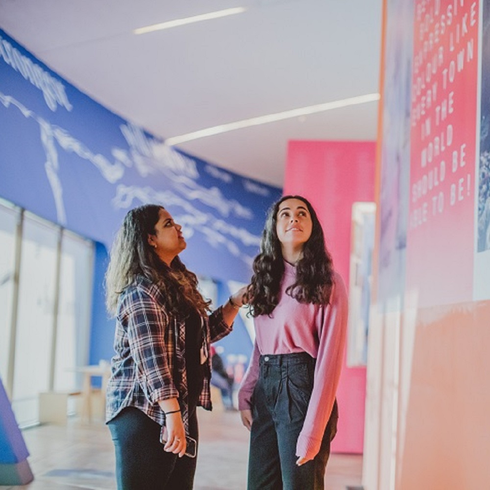 Two female students in a coridoor looking at a art work
