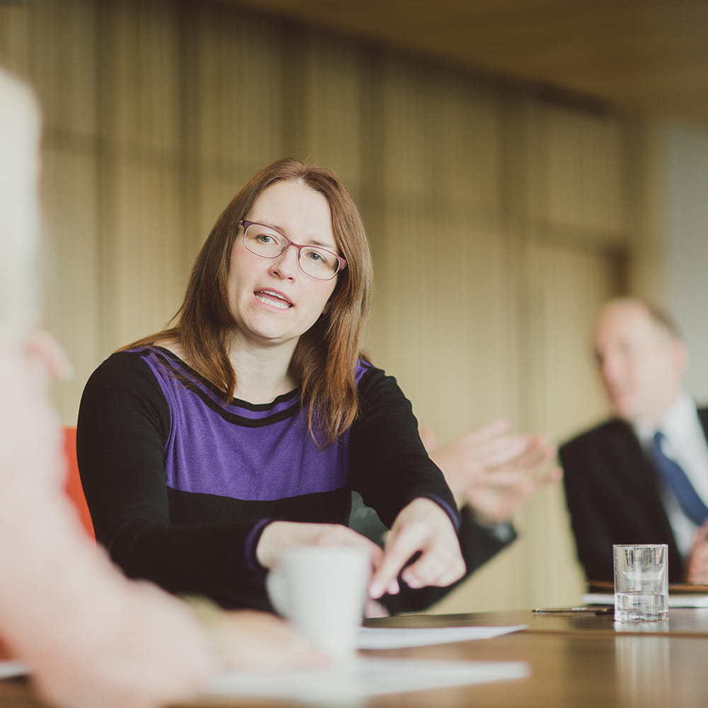 A lady wearing glasses discussing information on a conference table