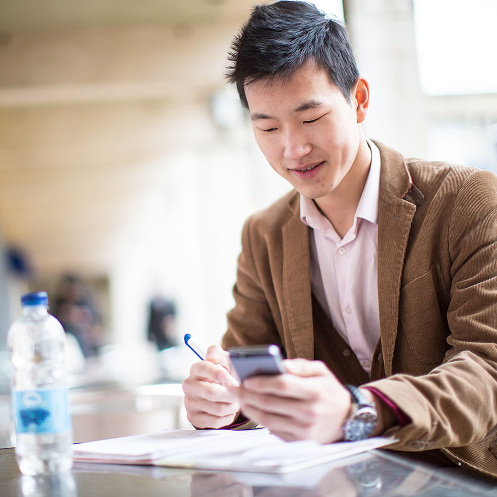 A man working at a desk looking at a mobile phone.