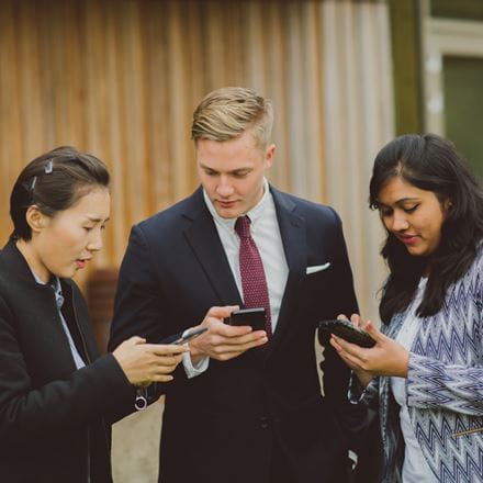 Three people, smartly dressed, using mobile phones.