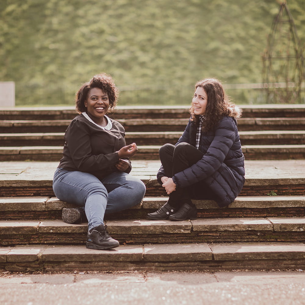 Two female students sitting on some steps outside talking