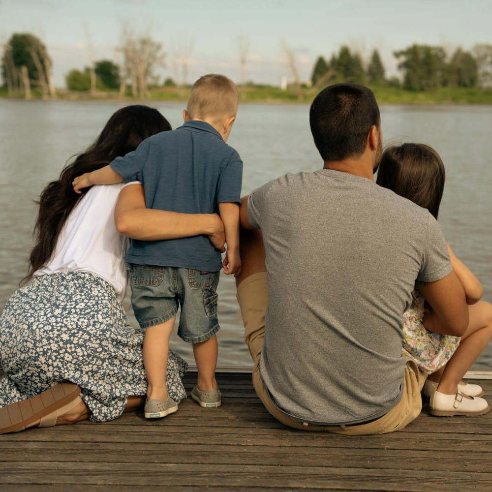 Two parents with a son and daughter, sitting on some decking looking out over a body of water.